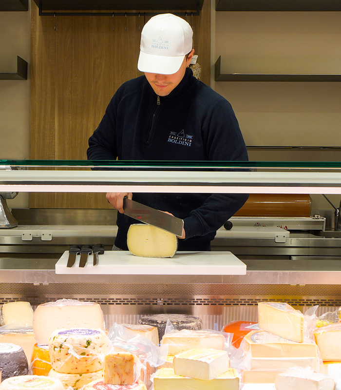 persona che taglia formaggio dietro un banco frigo
